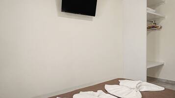 Une chambre avec un lit, un téléviseur à écran plat fixé au mur et une armoire blanche contenant des vêtements suspendus.