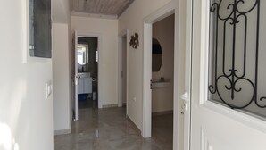 Un pasillo con techo de madera, una puerta blanca con diseño metálico y una cocina visible al fondo.