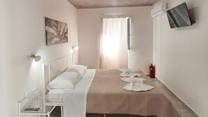 Un dormitorio con techo de madera, cama con ropa blanca, televisor montado y extintor.