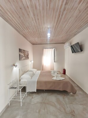 A bedroom with a wooden ceiling, a bed with white bedding, a mounted TV, and a fire extinguisher.