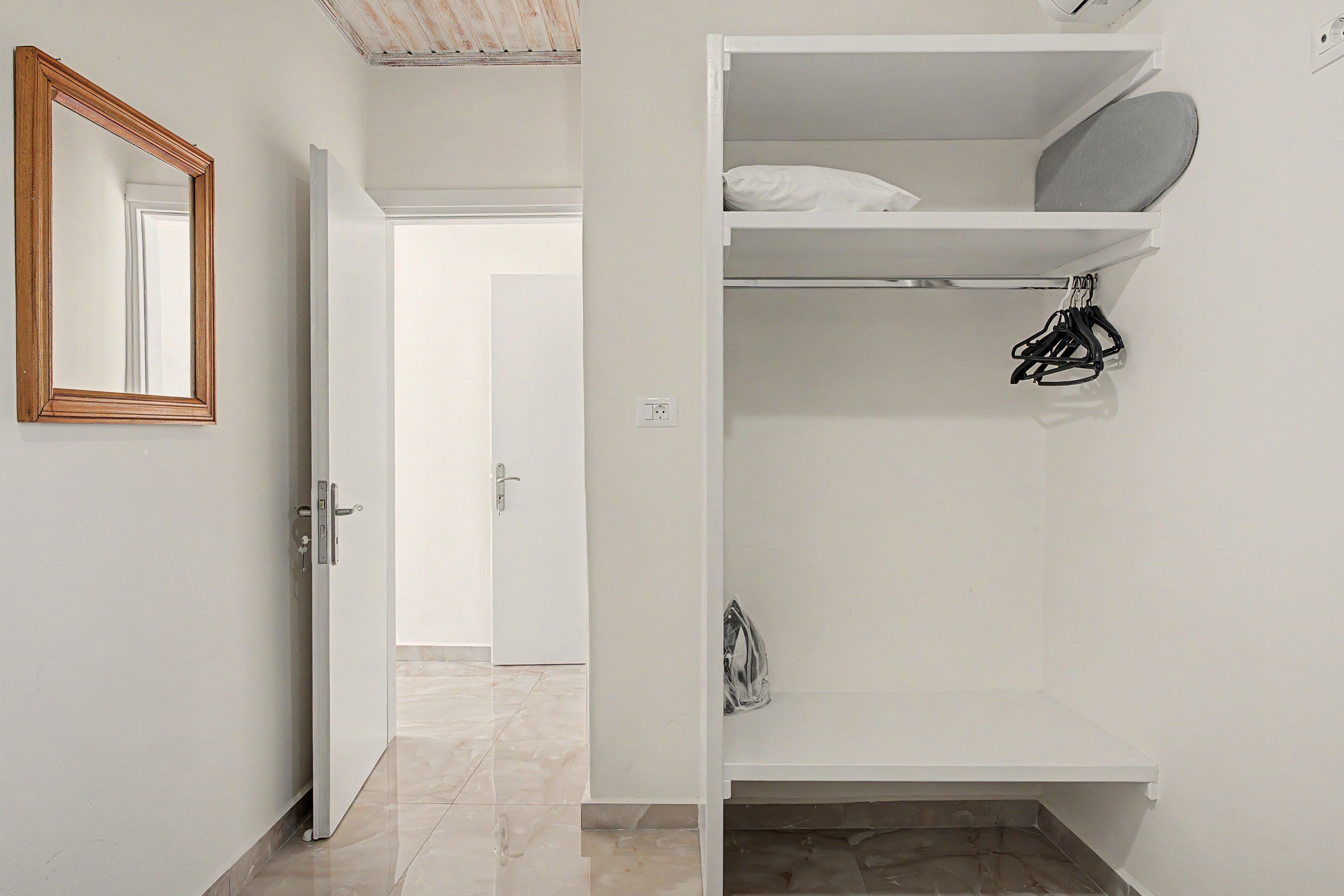 A white room with a door, a mirror, and a closet with shelves and hanging items.