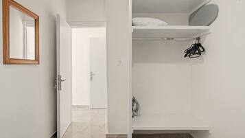 A white room with a door, a mirror, and a closet with shelves and hanging items.