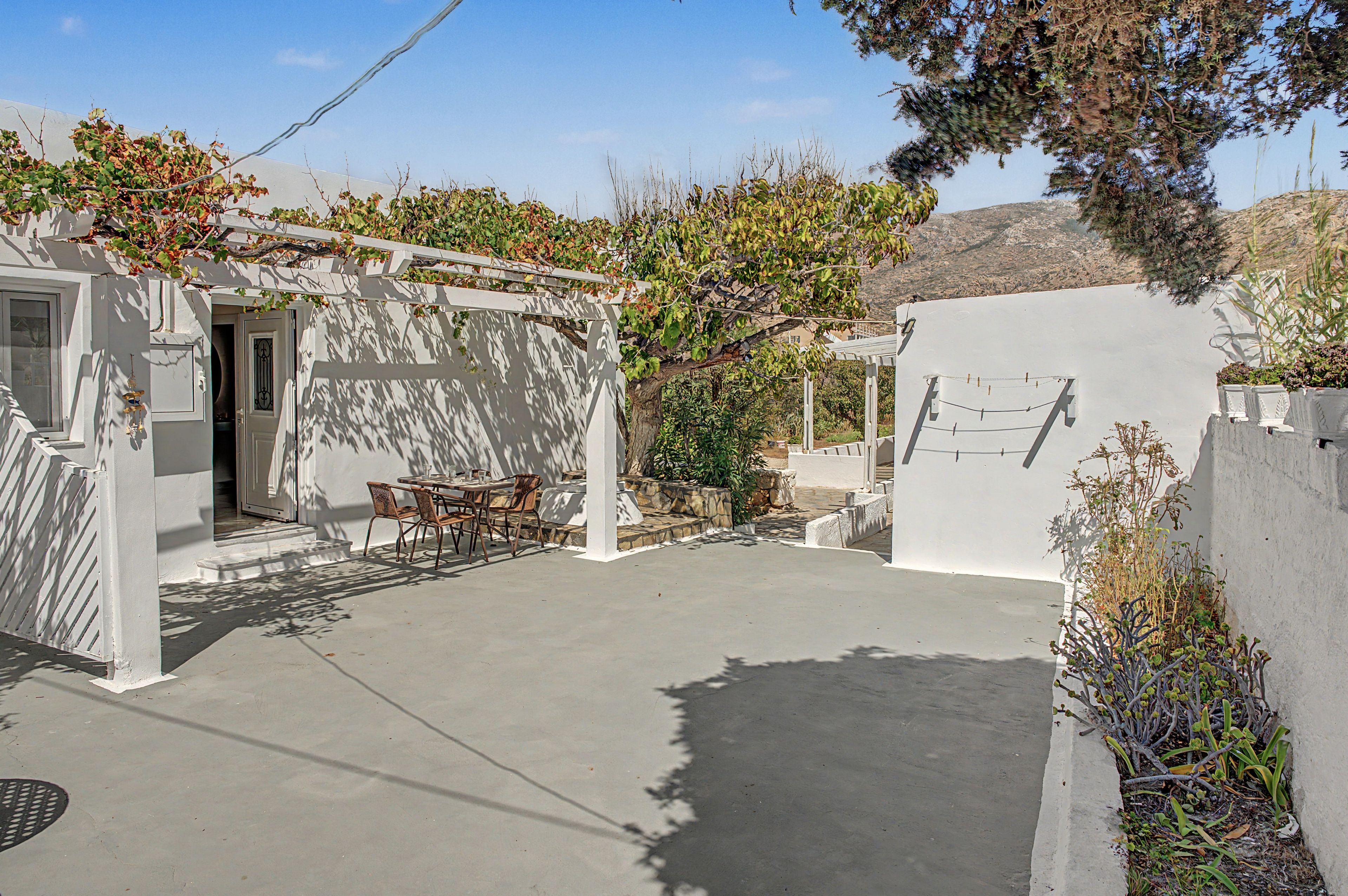 A courtyard with a white pergola, a table with chairs, and a stone wall.