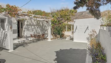 A courtyard with a white pergola, a table with chairs, and a stone wall.