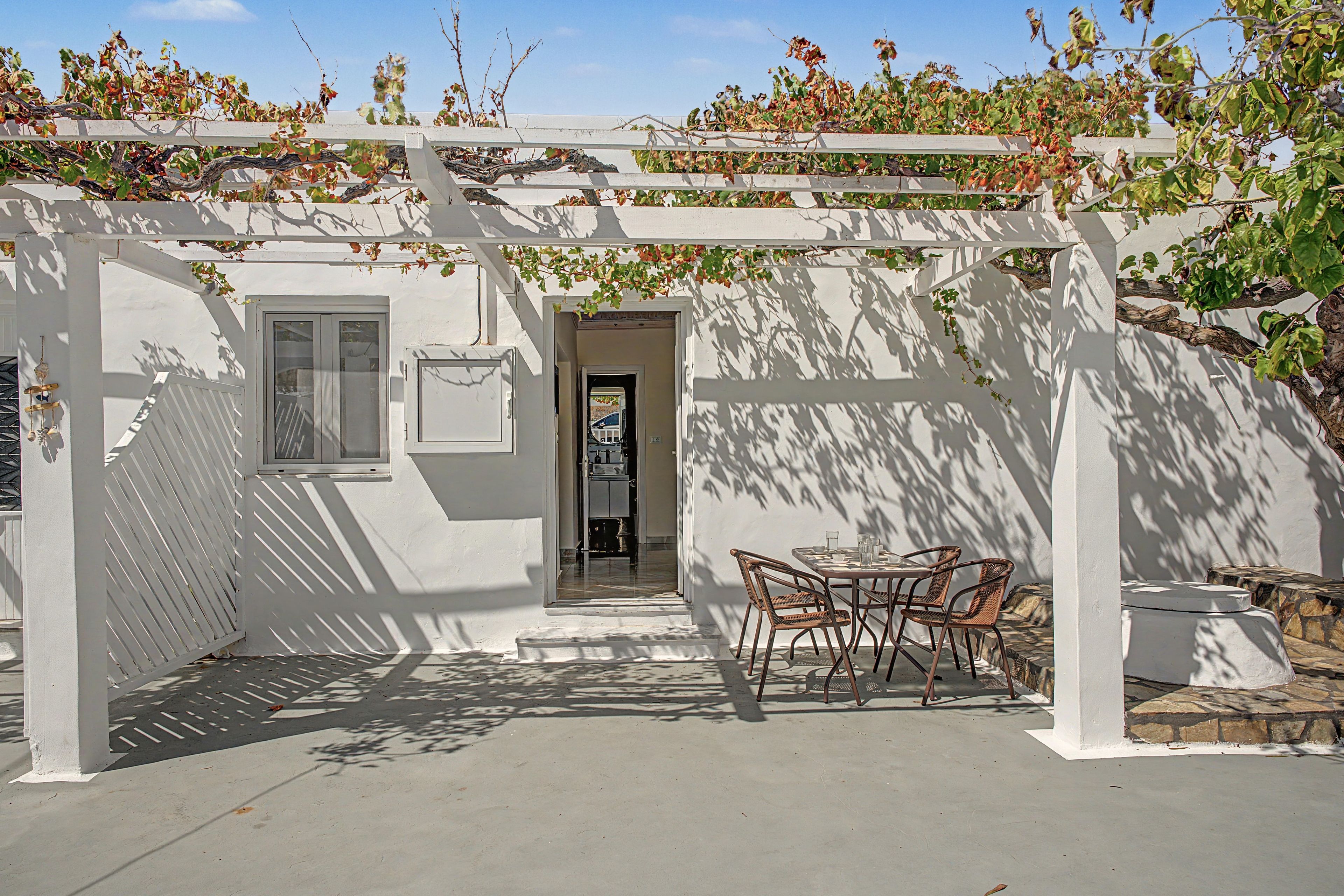 A covered patio area with a table and chairs, a white pergola, and a door leading to an interior space.