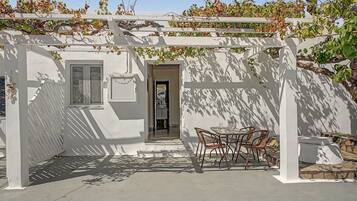 A covered patio area with a table and chairs, a white pergola, and a door leading to an interior space.