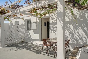 Un espace extérieur abrité, aménagé avec une table et des chaises, une pergola blanche et un bâtiment doté d’une fenêtre et d’une porte.