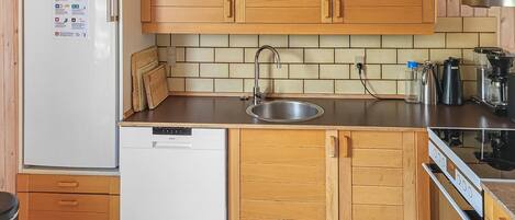 A compact kitchen with wooden cabinets, a stainless steel sink, a white dishwasher, and a coffee maker.