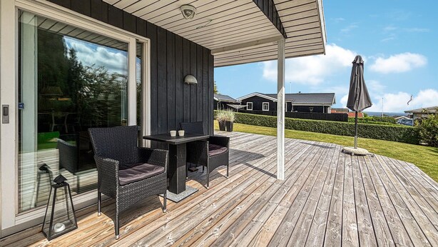 Een overdekt buitengebied met rieten meubels, een tafel en een parasol.