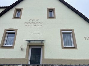 A two-story building with a beige facade, numbered 40, and a sign indicating 'Brigitte Fremdenzimmer' with a telephone number.