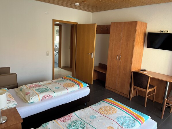 A hotel room with two beds, a desk, a wardrobe, and a TV.
