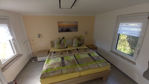 Un dormitorio con cama, mesita de noche, lámpara, ventana y un cuadro en la pared.