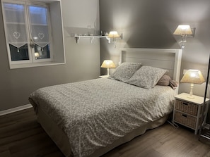 Une chambre à coucher comprenant un lit, des lampes de chevet, une table de chevet, une fenêtre avec des rideaux et une étagère fixée au mur.