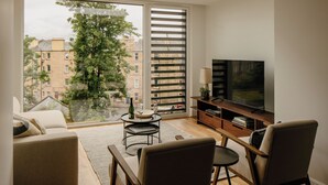 Una sala de estar moderna con un ventanal grande, un televisor de pantalla plana, un sofá, una mesita de centro y una estantería.
