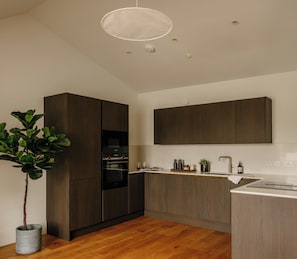 A modern kitchen with dark wood cabinets, a built-in oven, a white countertop, and a hanging light fixture.