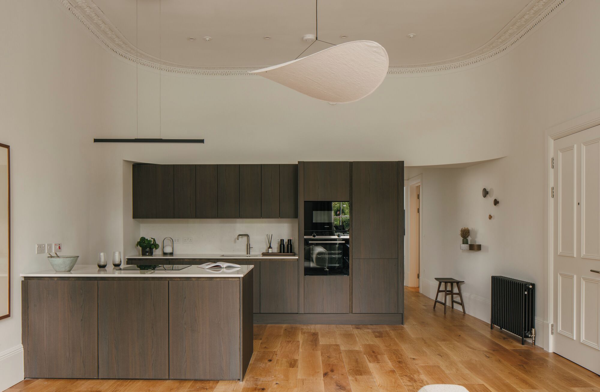 A modern kitchen with dark wood cabinets, a central island, and a large pendant light.