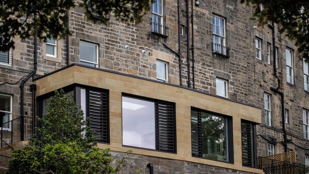 Un edificio moderno con fachada de piedra, ventanas amplias y techo plano.