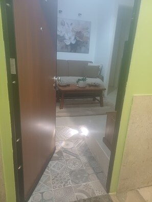 Un couloir avec un sol à motifs, une porte en bois et un canapé beige agrémenté d’un coussin et d’une petite plante.