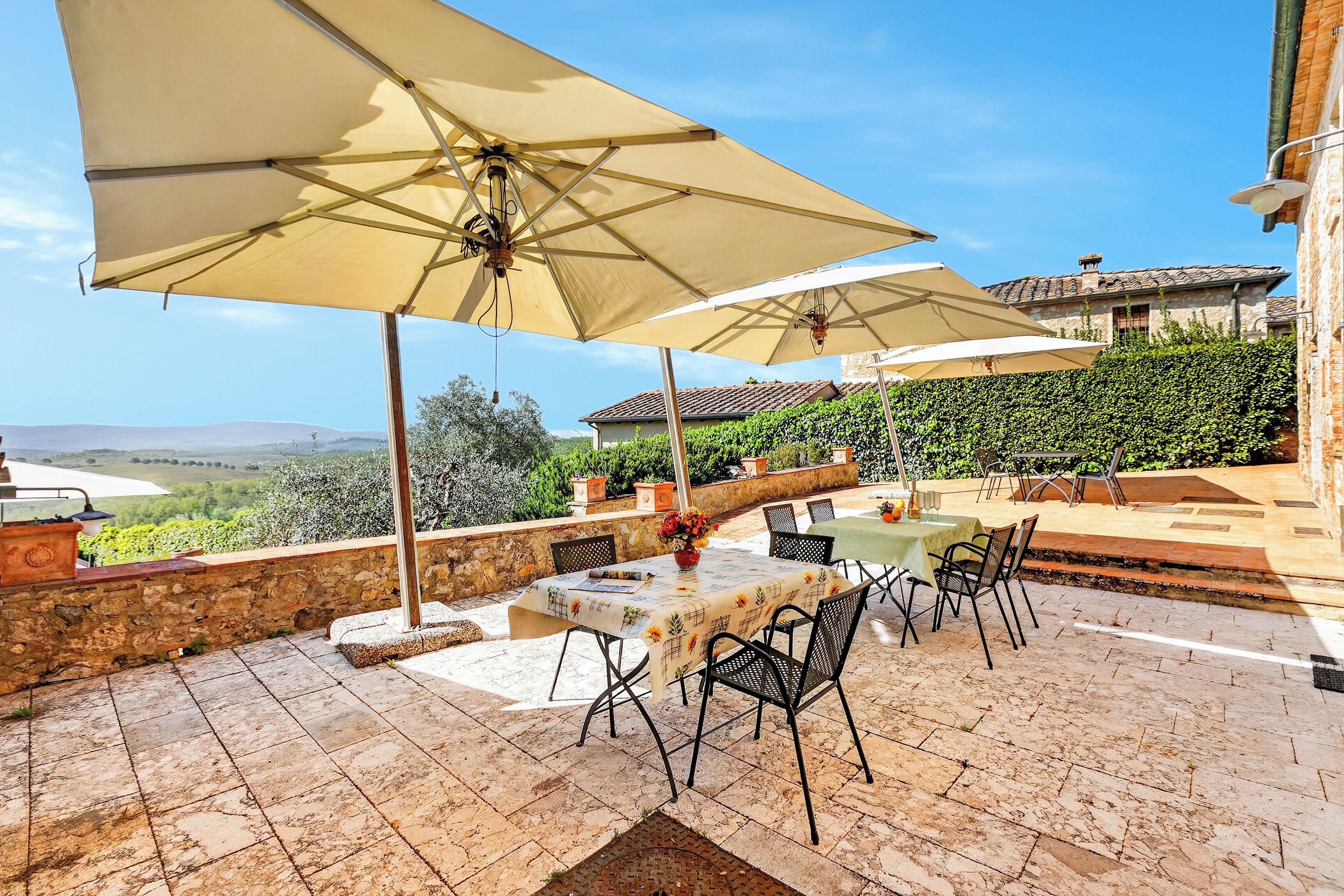 An outdoor patio with a table and chairs, two large umbrellas, and a view of the countryside.