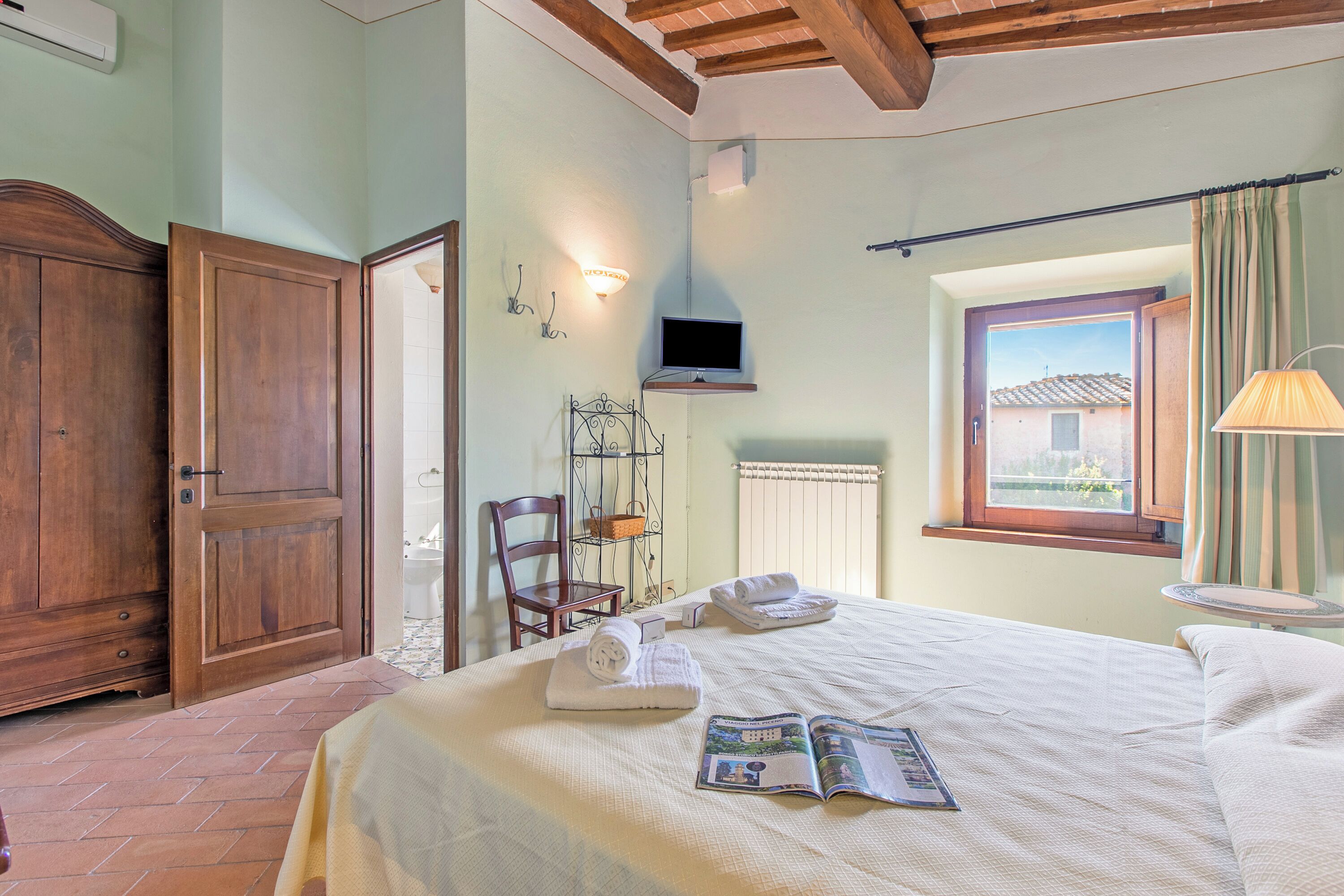 Ein Schlafzimmer mit Bett, Sessel, Fernseher, Fenster und Kleiderschrank.