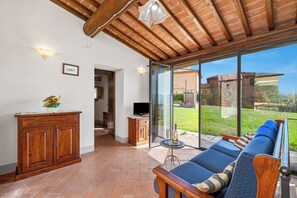 Une pièce avec un plafond en bois, un canapé avec des coussins, un meuble, une télévision et une porte vitrée donnant sur l’extérieur.