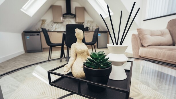 A modern living room with a glass coffee table, a potted succulent, a decorative figurine, and a set of black incense sticks.