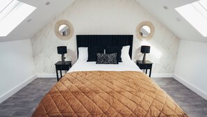 A bedroom with a large bed, two bedside tables with lamps, a black headboard, and a skylight.
