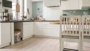 A modern kitchen with white cabinets, a wooden countertop, and a dining area with a white chair. - Villa cosy proche Valenciennes (La Sentinelle)