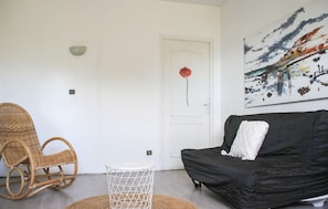 A room with a black sofa, a wicker chair, a small white table, and a door with a red flower decoration. - Villa cosy proche Valenciennes (La Sentinelle)