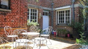 A brick building with a patio area featuring a round table and four chairs. - Villa cosy proche Valenciennes (La Sentinelle)