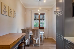Un comedor con mesa de madera y sillas de mimbre, una ventana con cortinas, y una cocina moderna con refrigerador.