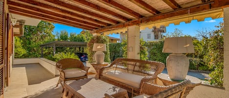 An outdoor patio with wicker furniture, a pergola, and a view of greenery and buildings.