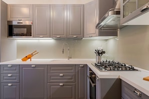A modern kitchen with grey cabinets, a built-in oven, a gas stove, and a stainless steel range hood.