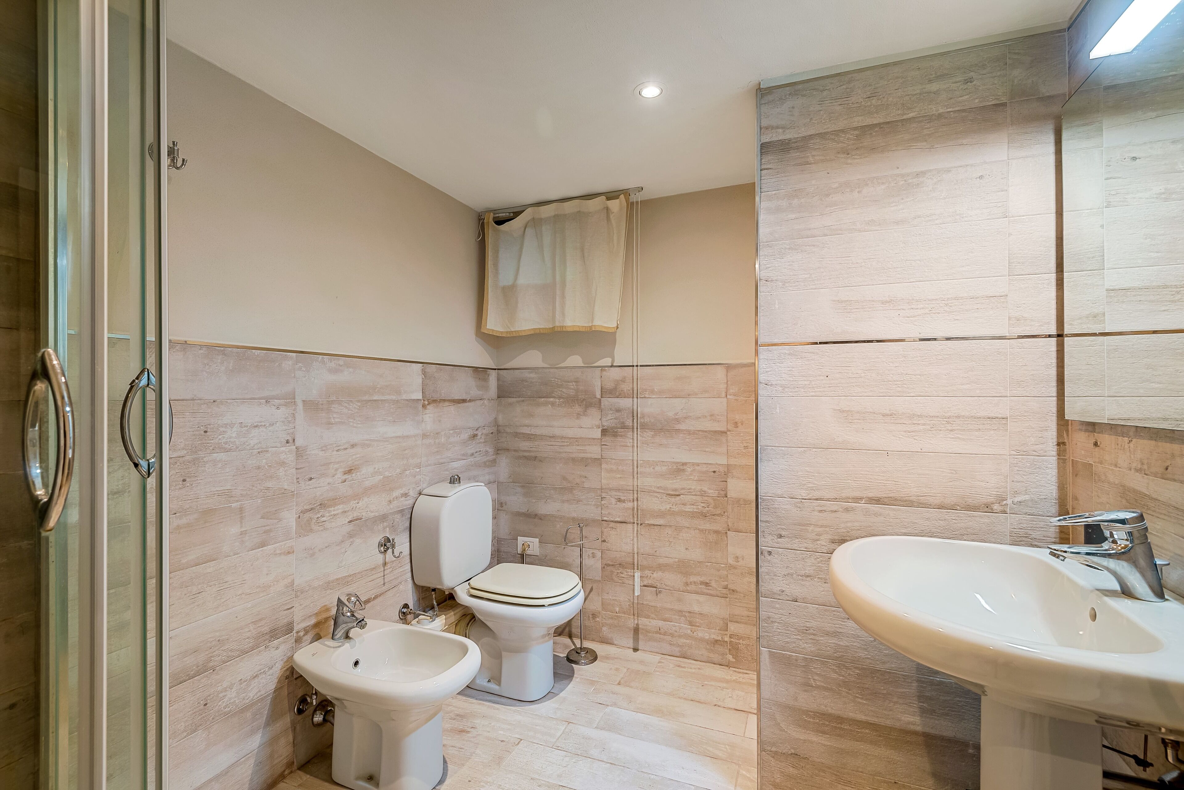 A modern bathroom with a glass shower enclosure, a toilet, bidet, and a sink.