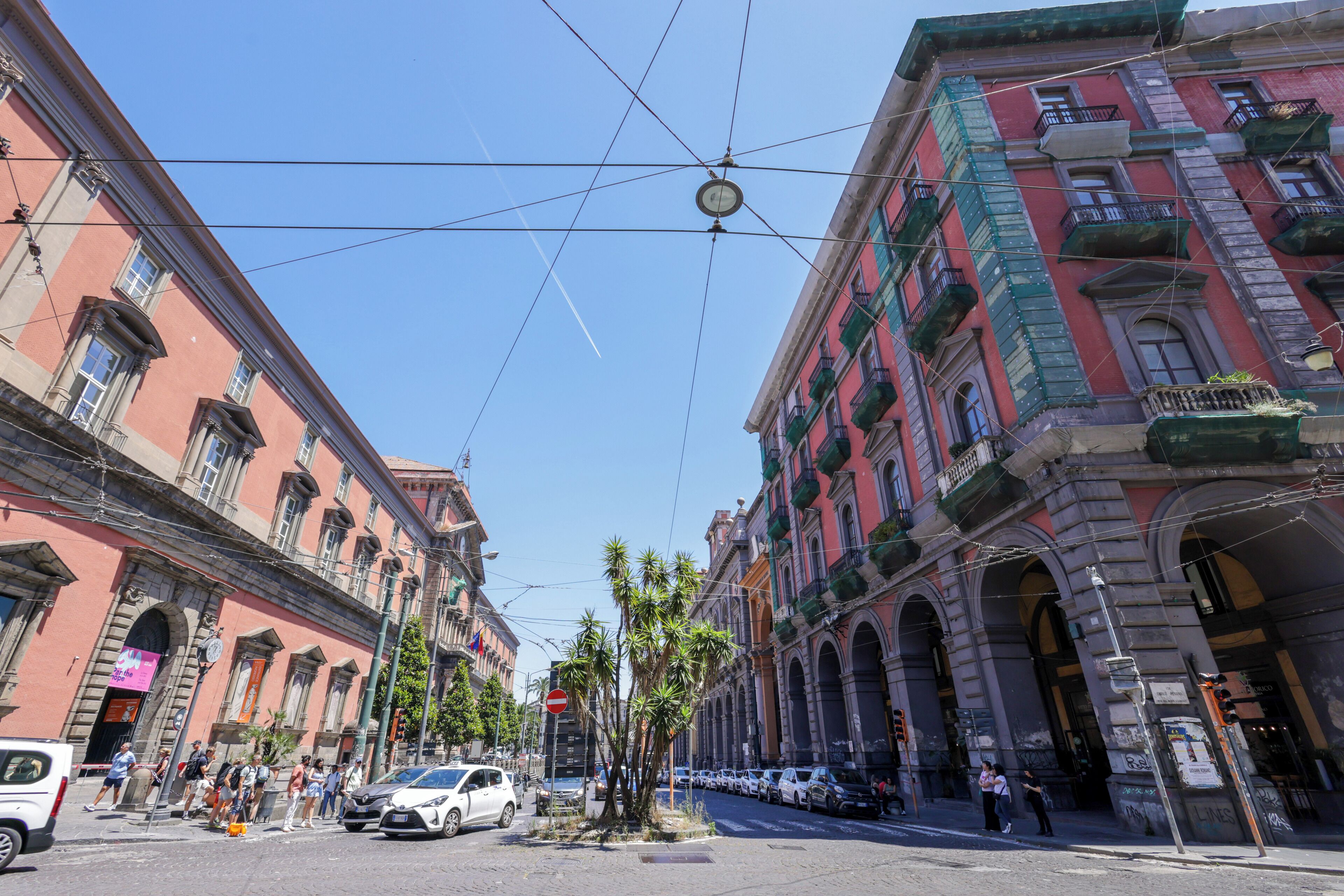 A street with historic buildings, a tram line, and parked cars.