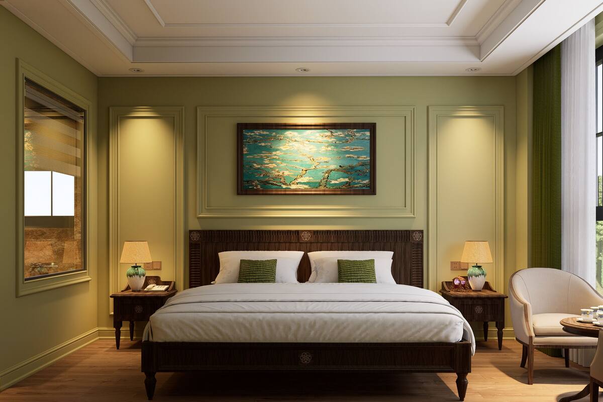 A bedroom with a large bed, two bedside tables, a chair, a painting, and a window with curtains.