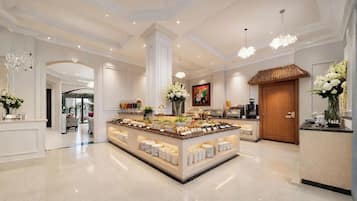 A spacious hotel lobby with a central buffet area, a reception desk, and a large wooden door.