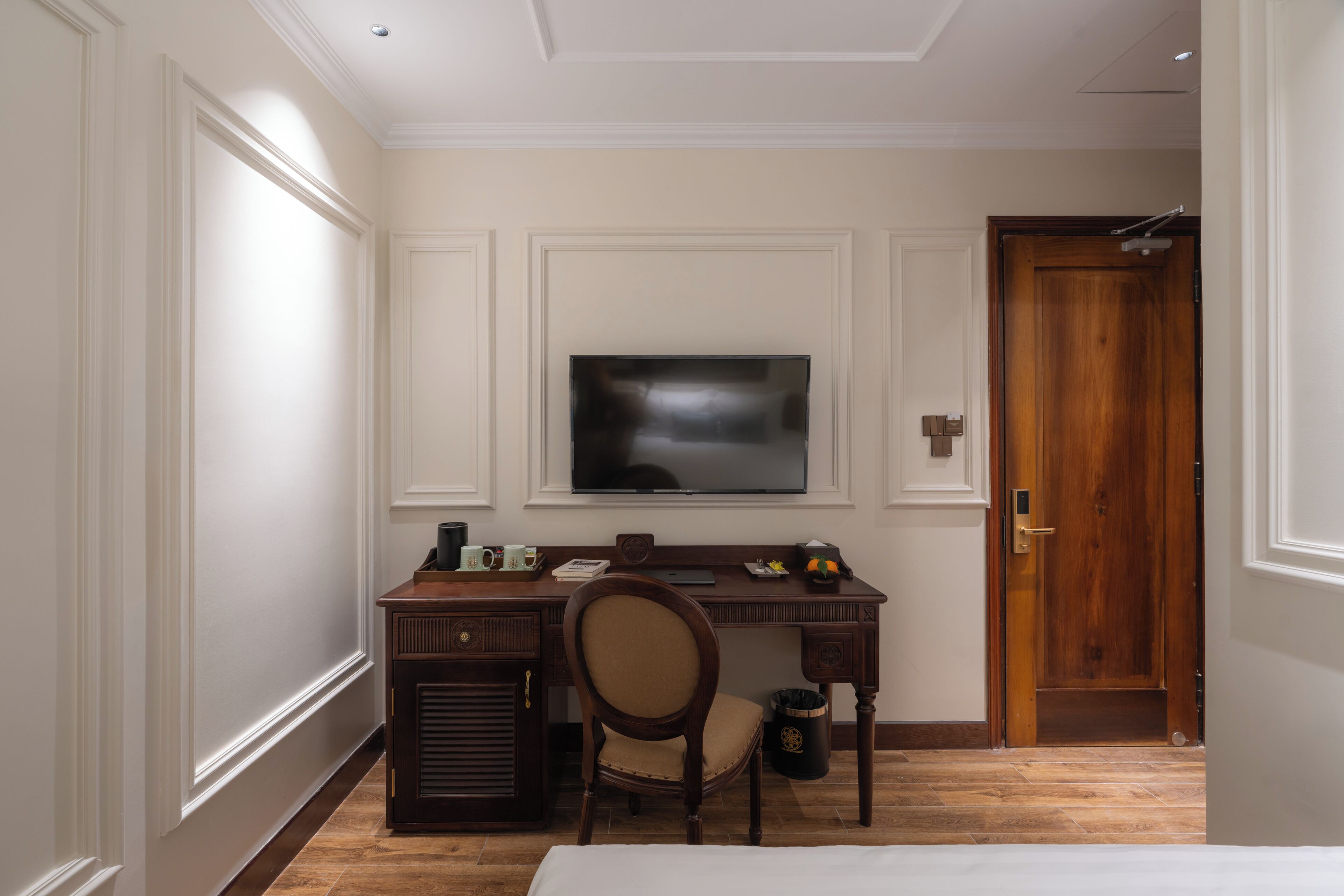 A hotel room with a wooden desk, a television, a chair, and a door.