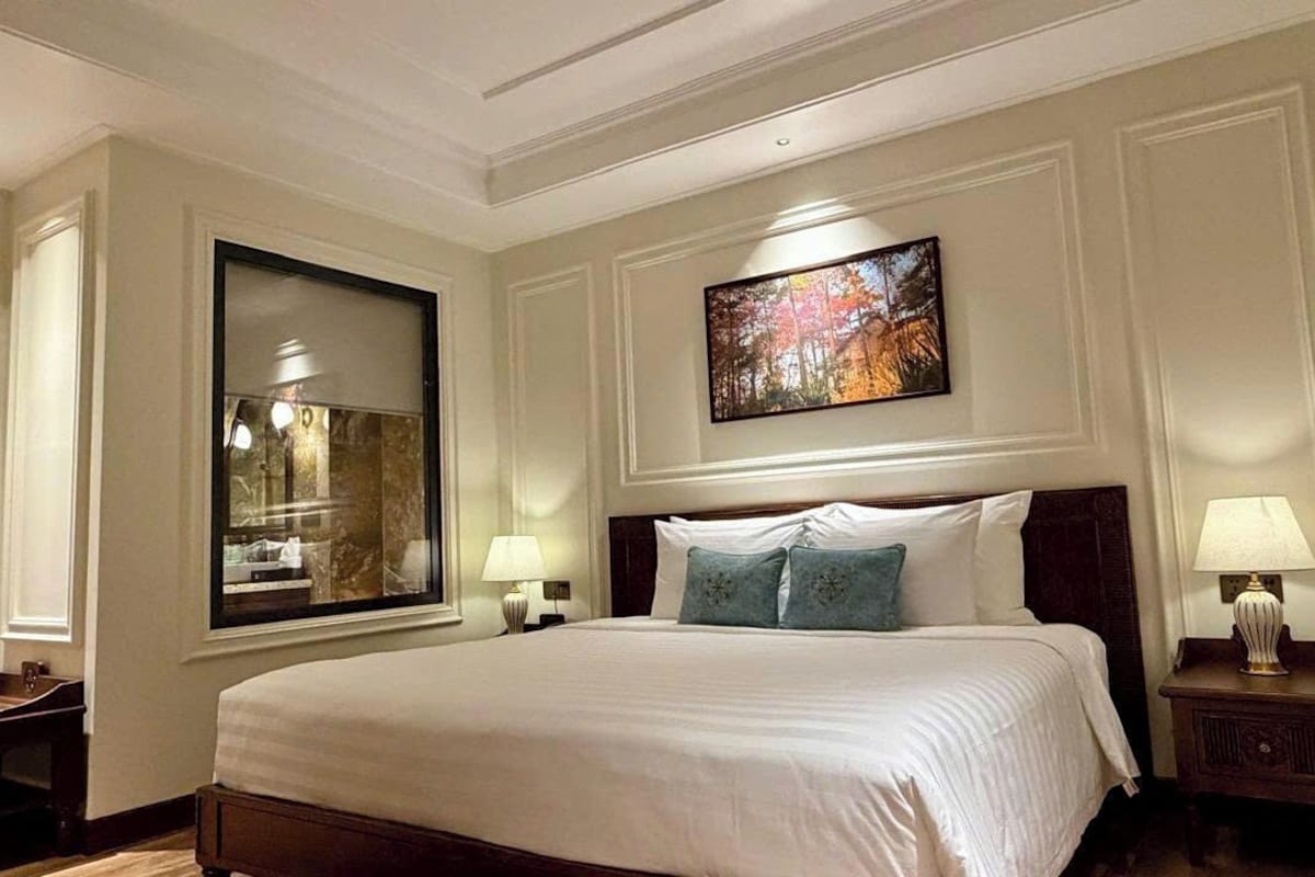 A hotel room with a large bed, two bedside tables with lamps, a large mirror, and a framed picture on the wall.