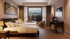 A hotel room with a large bed, a desk, a chair, a TV, and a painting. - Dalabiang Hotel (Xuan Huong - Da Lat)