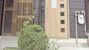 A two-story building with a wooden door, a balcony with plants, and a metal railing. - Dc Sakura Hotel - Tenjin Beppu (Osaka)