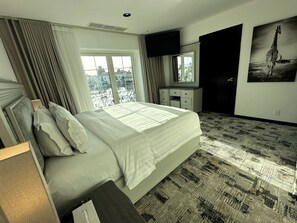 A hotel room with a bed, a dresser, a mirror, a window with curtains, and a painting of a giraffe. -  Sunset Beach Resort for Entertainment (Eastern Province)