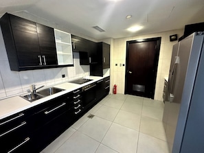 A modern kitchen with black cabinets, white countertops, a double sink, and a built-in oven. -  Sunset Beach Resort for Entertainment (Eastern Province)