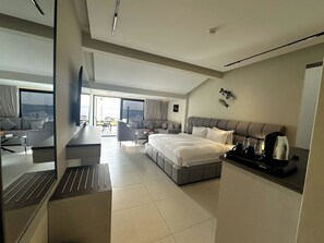A modern hotel room with a bed, a dining area, a TV, and a view of the sea. -  Sunset Beach Resort for Entertainment (Eastern Province)