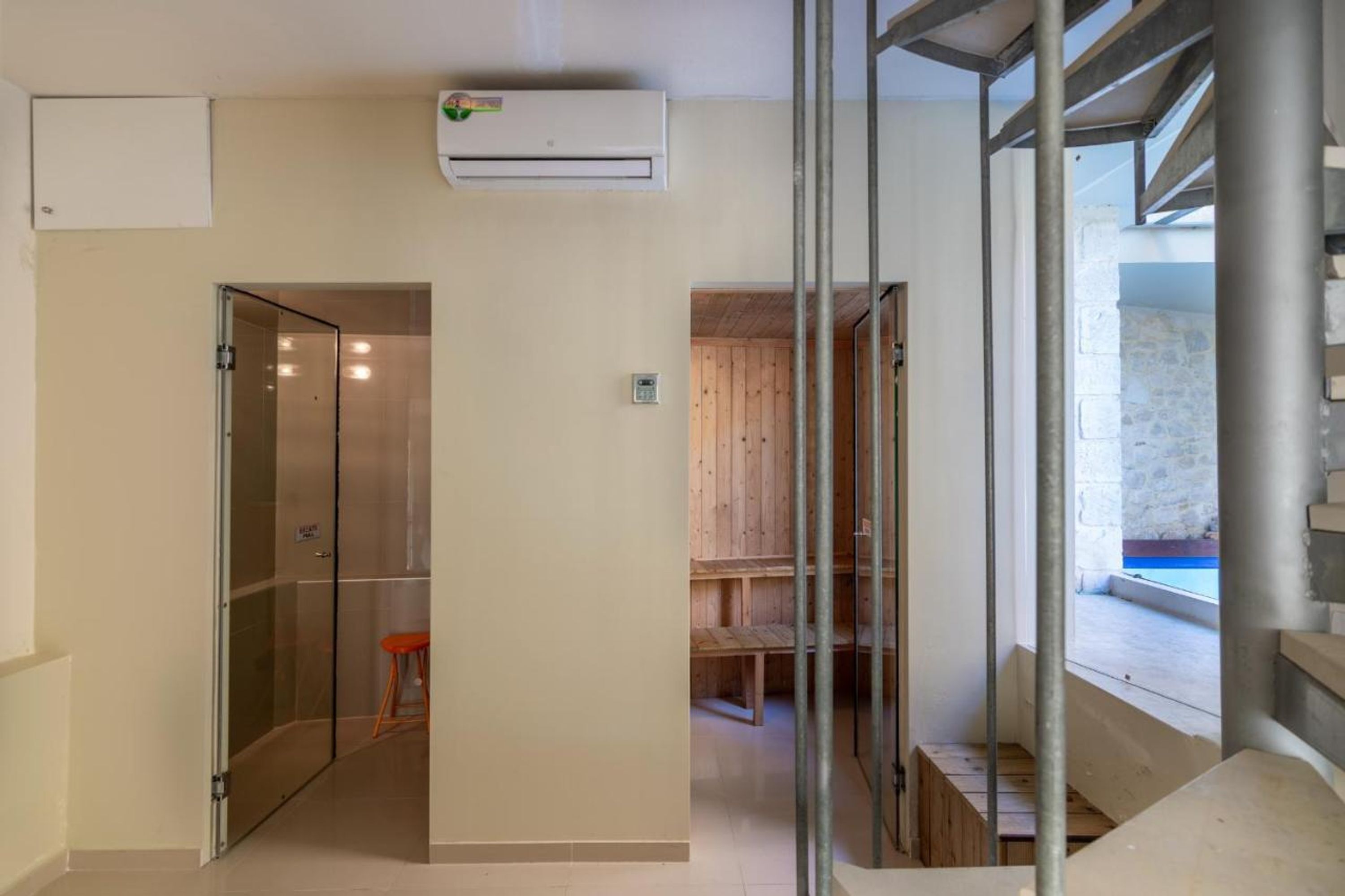 A modern interior with a glass door leading to a shower area, a wooden sauna, and a view of a stone wall and outdoor area.
