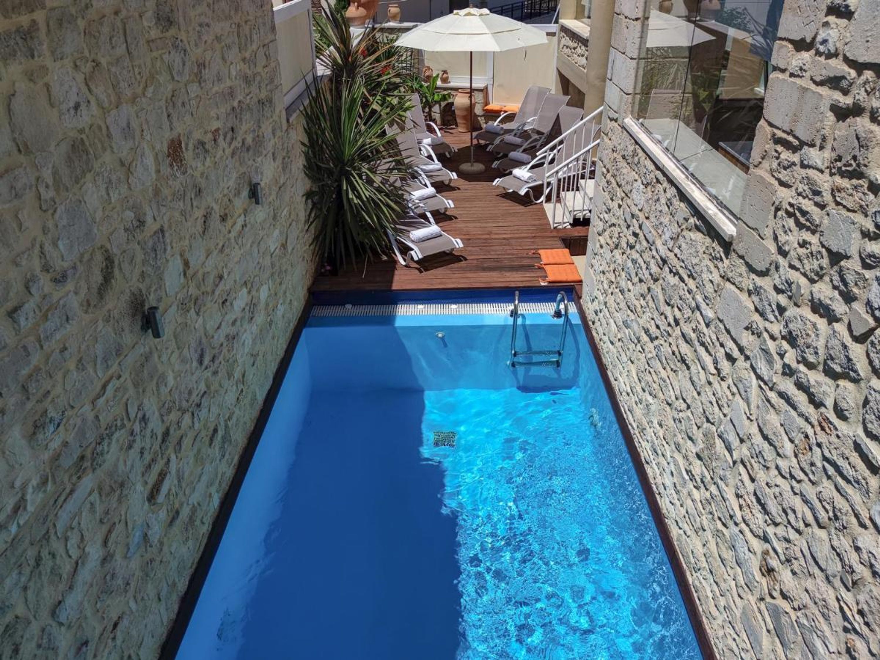A swimming pool with a wooden deck, lounge chairs, and a stone wall.