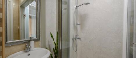 A bathroom with a glass-enclosed shower, a sink, and a mirror.