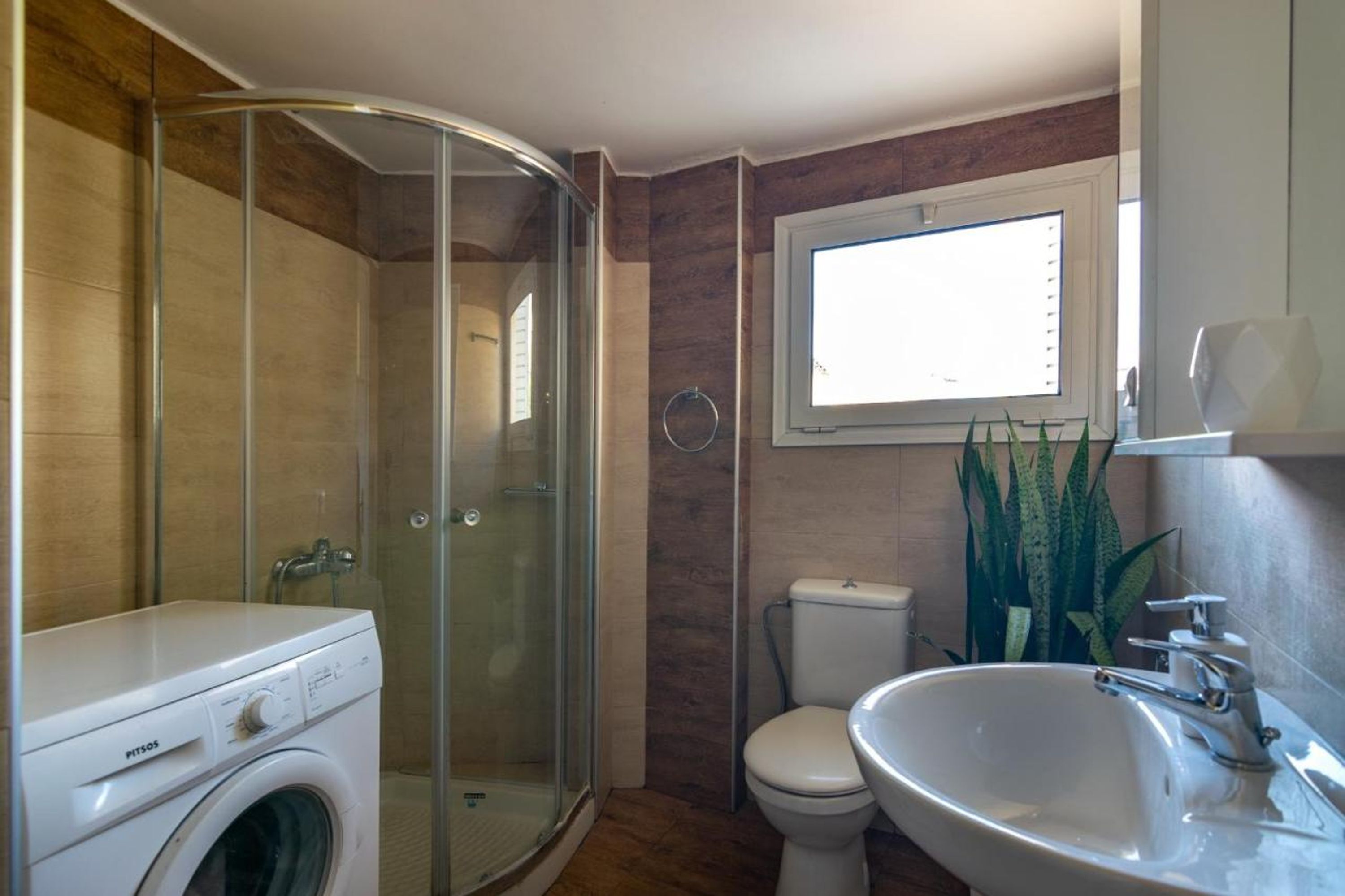 Un bagno con cabina doccia in vetro, lavatrice, water e lavandino.