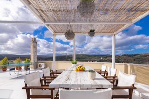 Eine Dachterrasse mit Holztisch, Stühlen, hängenden Körben und Blick auf die Landschaft.