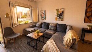 A living room with a sofa, a coffee table, a chair, and a window with a view. - Stylish Flat in Puerto Banús - Steps to Marina (Marbella)